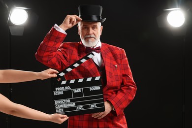 Photo of Senior actor performing role while second assistant camera holding clapperboard on stage. Film industry