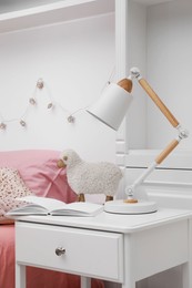 Photo of Lamp on white nightstand in cozy bedroom