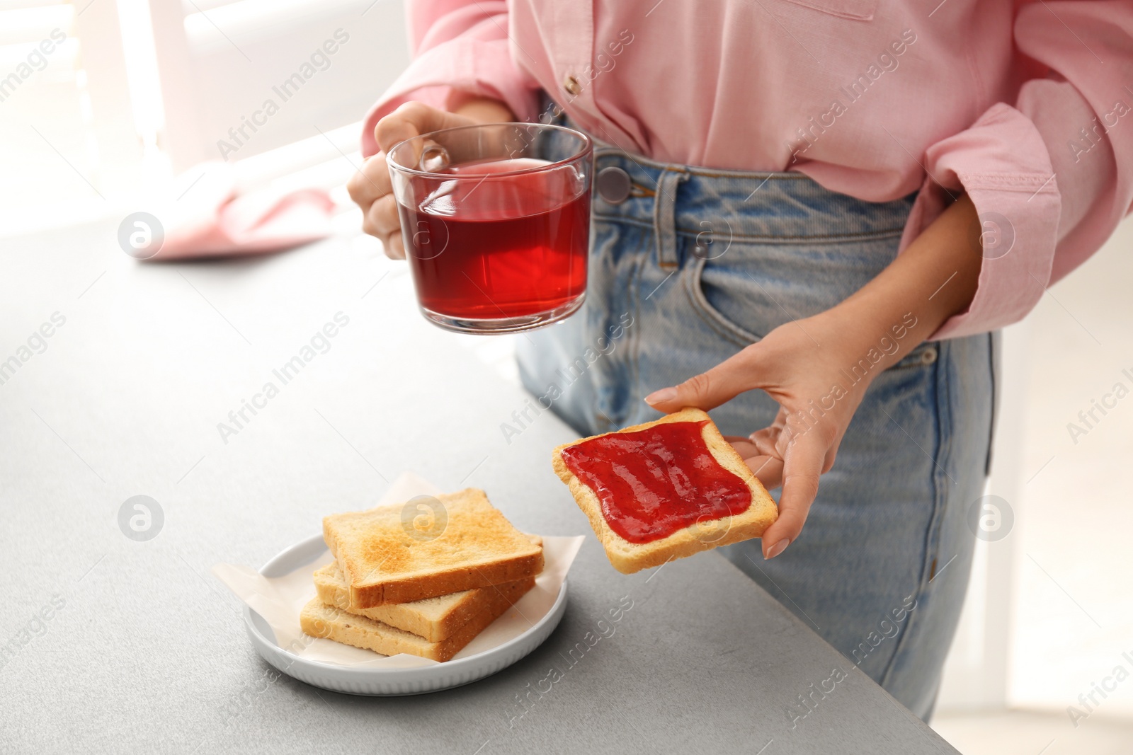 Photo of Woman having tasty breakfast with toast and raspberry tea at home, closeup. Morning routine