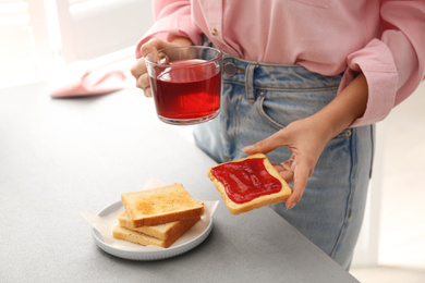 Photo of Woman having tasty breakfast with toast and raspberry tea at home, closeup. Morning routine