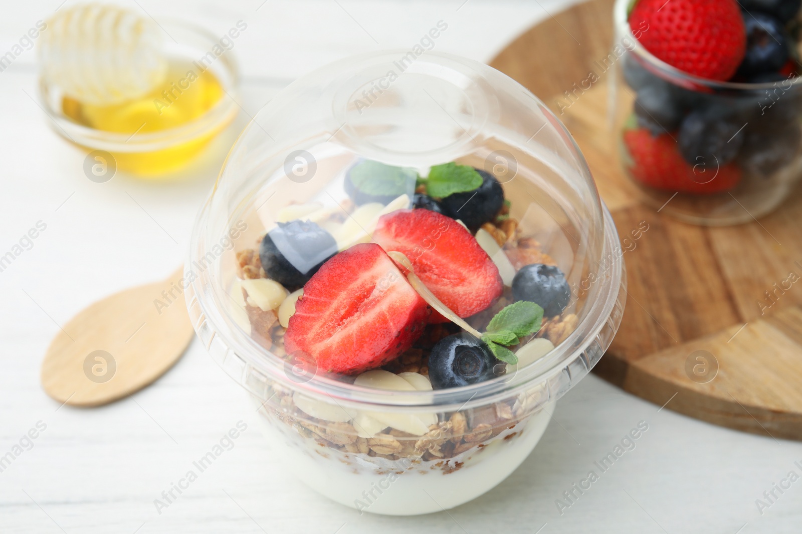 Photo of Tasty granola with berries, yogurt and almond flakes in plastic cup on white table, closeup