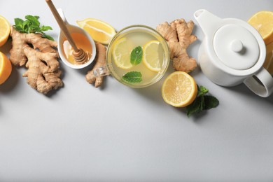 Delicious ginger tea and ingredients on light grey background, flat lay. Space for text