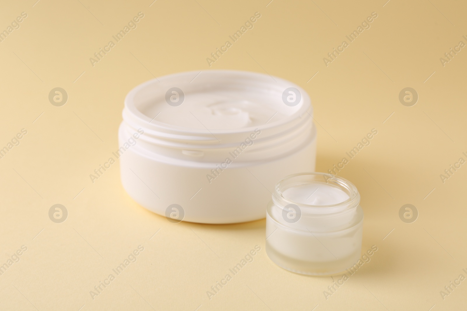 Photo of Moisturizing cream in open jars on beige background. Body care products