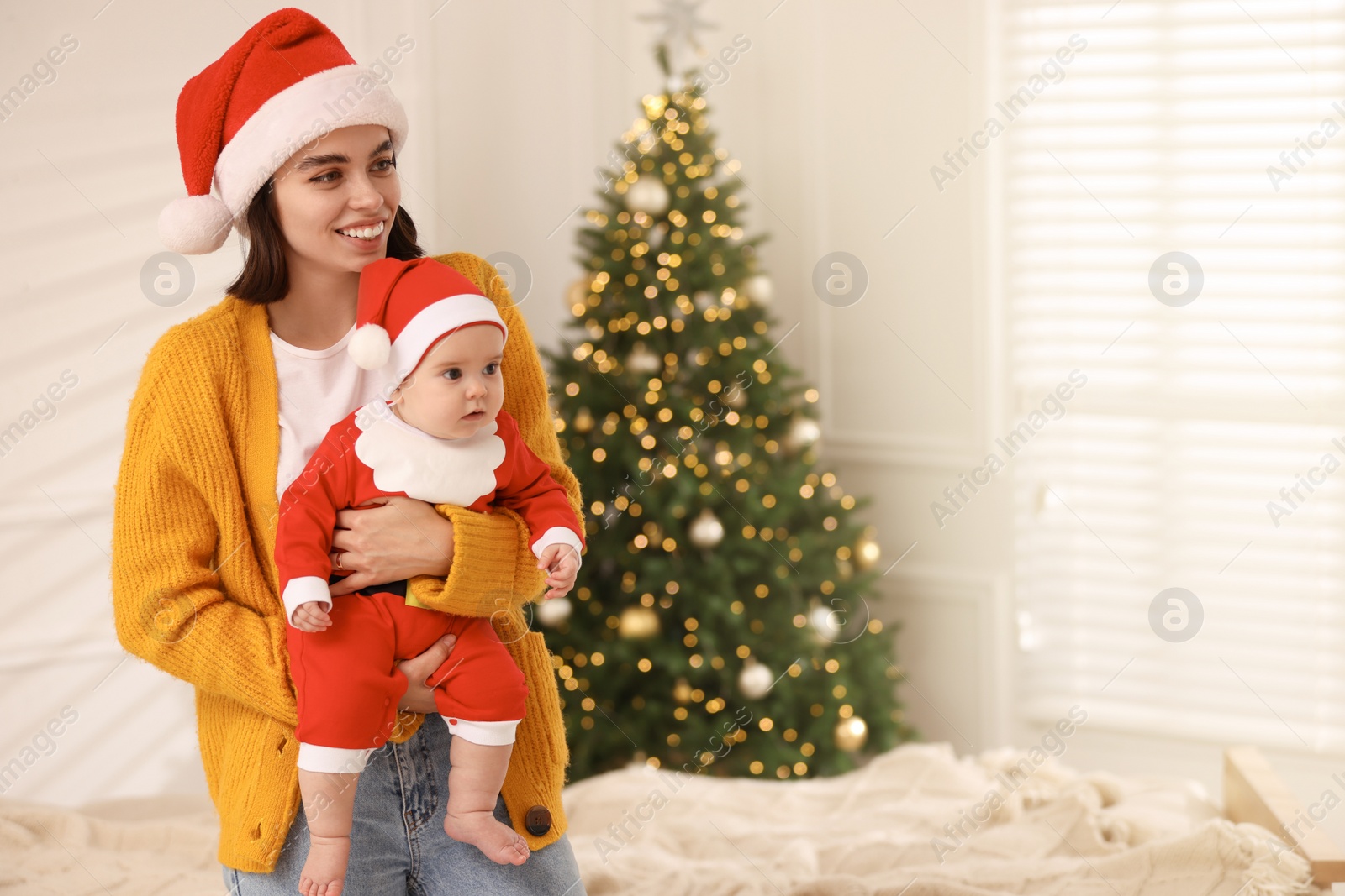 Photo of Happy young mother with her cute baby against blurred festive lights, space for text. Winter holiday