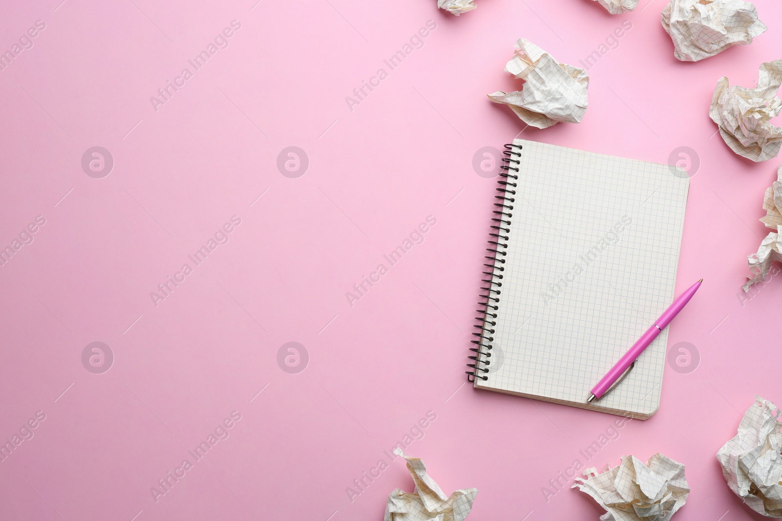 Photo of Notebook, pen and crumpled sheets of paper on light pink background, flat lay. Space for text