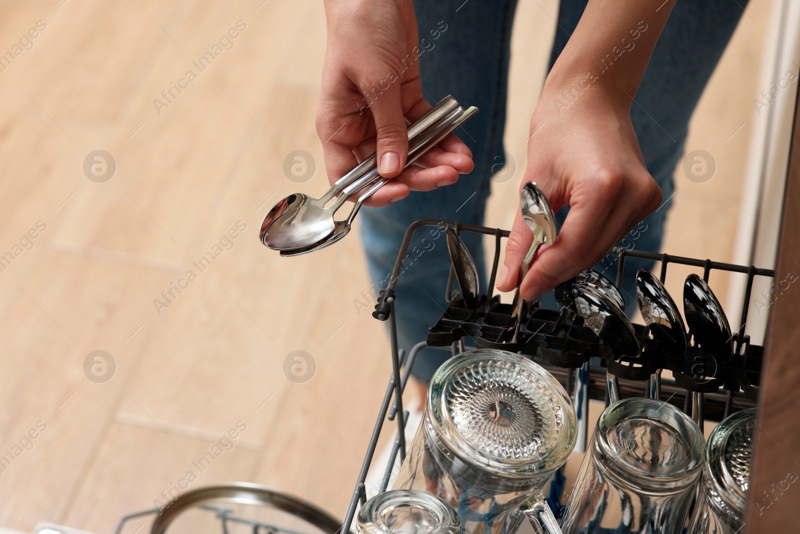 Photo of Woman loading dishwasher with glass and cutlery indoors, closeup