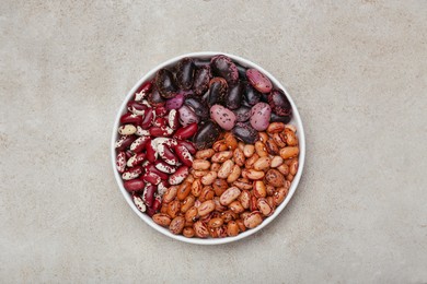 Photo of Bowl with different types of beans on light grey table, top view