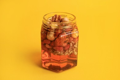 Photo of Different nuts and honey in jar on yellow background