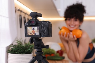 Photo of Food blogger explaining something while recording video in kitchen, focus on camera