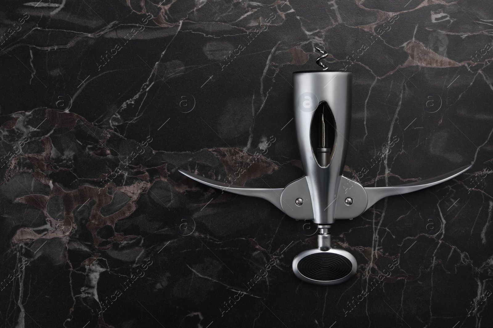 Photo of One wing corkscrew on black marble table, top view. Space for text