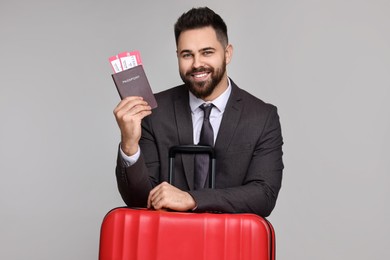 Happy businessman with passport, tickets and suitcase on grey background