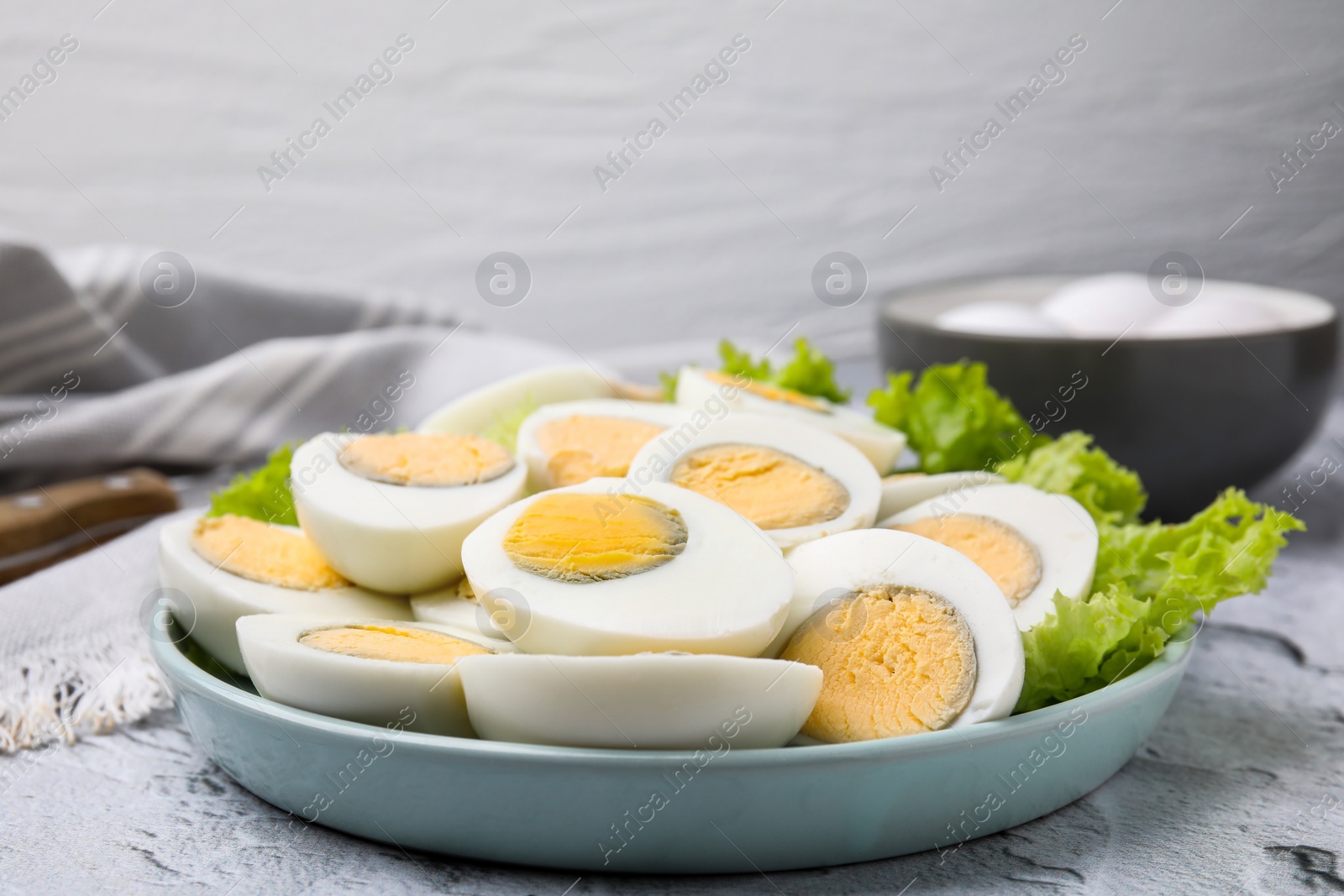 Photo of Fresh hard boiled eggs and lettuce on light grey textured table