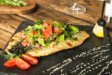 Photo of Delicious grilled fish with vegetables on slate plate