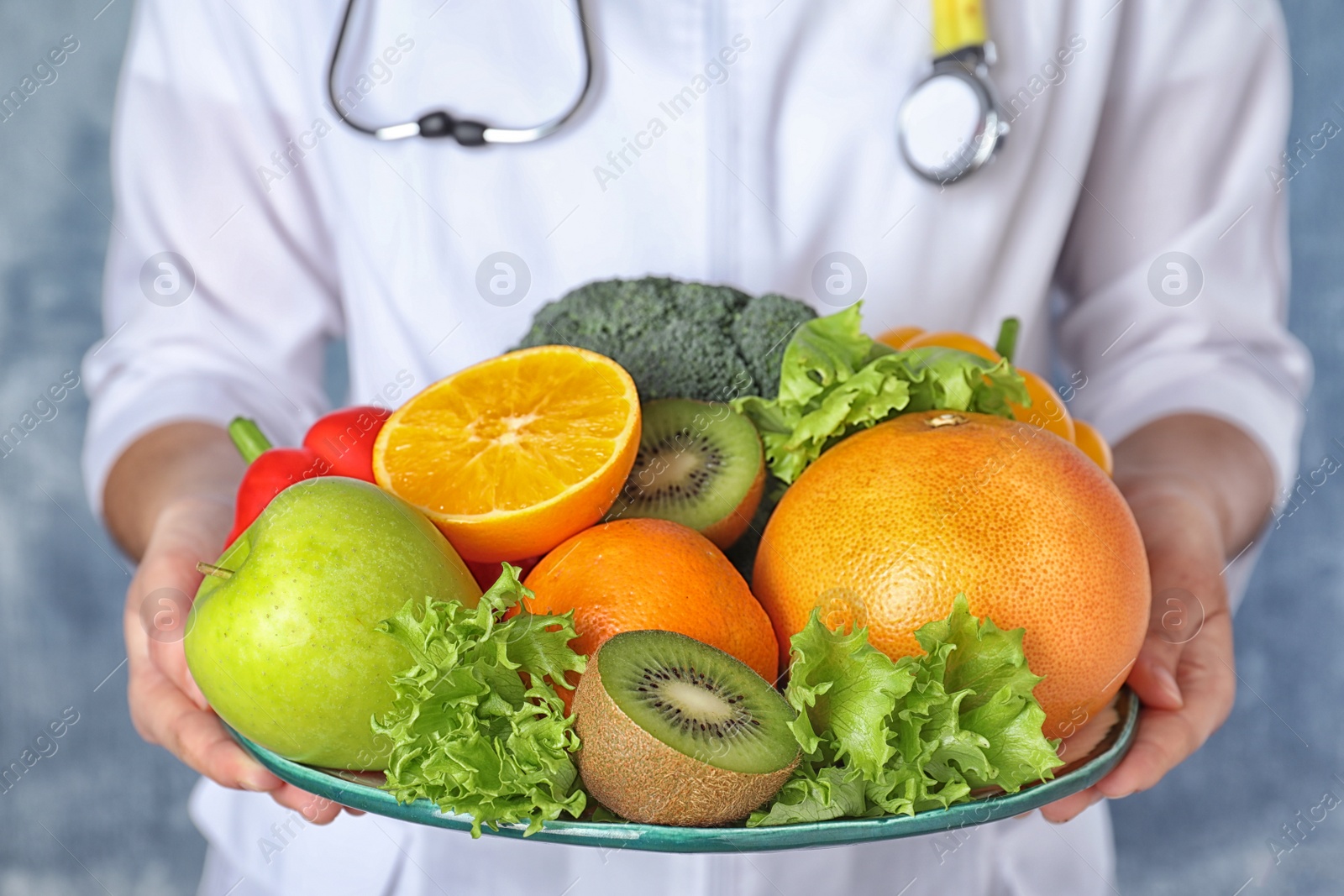 Photo of Female nutritionist with fruits and vegetables on light blue background, closeup