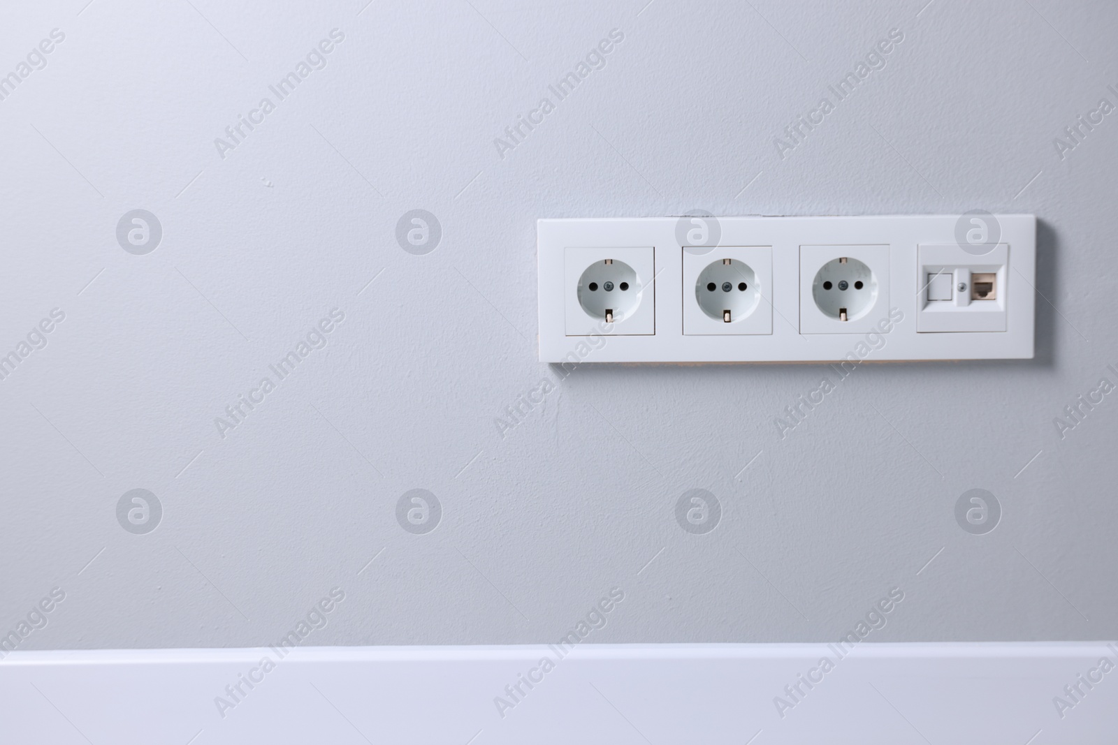 Photo of Electric power sockets on light grey wall indoors, space for text