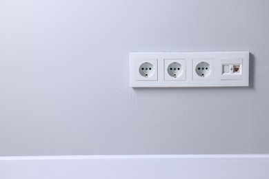 Electric power sockets on light grey wall indoors, space for text