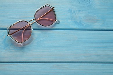 Photo of New stylish sunglasses on turquoise wooden table, top view. Space for text