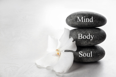Photo of Stones with words MIND, BODY, SOUL and orchid flower on light background. Zen lifestyle