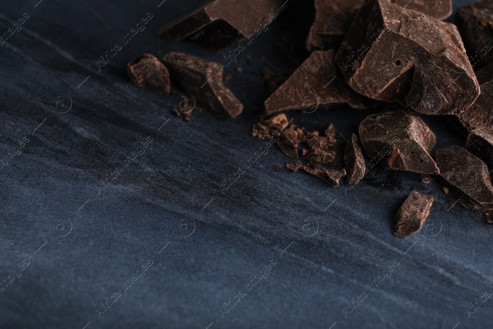 Photo of Pieces of dark chocolate on blue marble table, closeup. Space for text