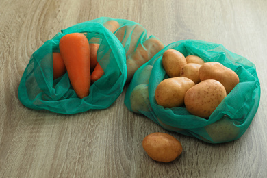 Net bags with vegetables on wooden table