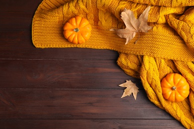 Photo of Orange knitted plaid with dry leaves and pumpkins on brown wooden table, flat lay. Space for text