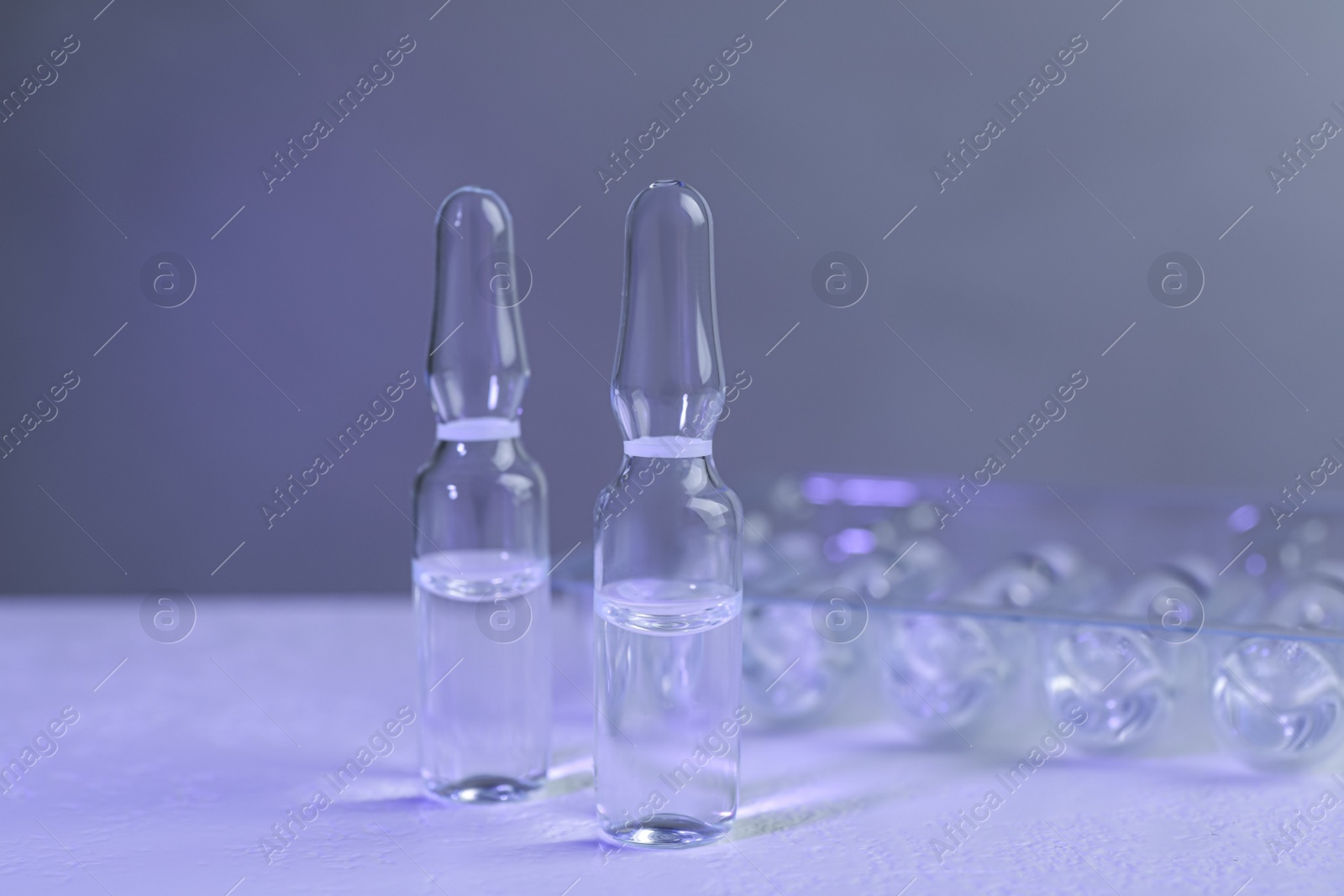 Photo of Pharmaceutical ampoules with medication on white table against grey background