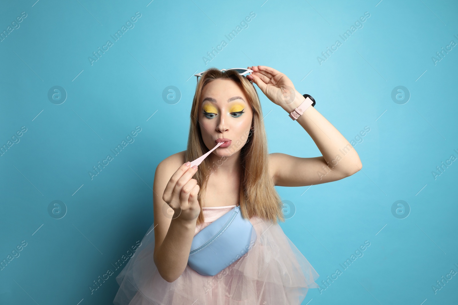 Photo of Fashionable young woman with bright makeup chewing bubblegum on light blue background