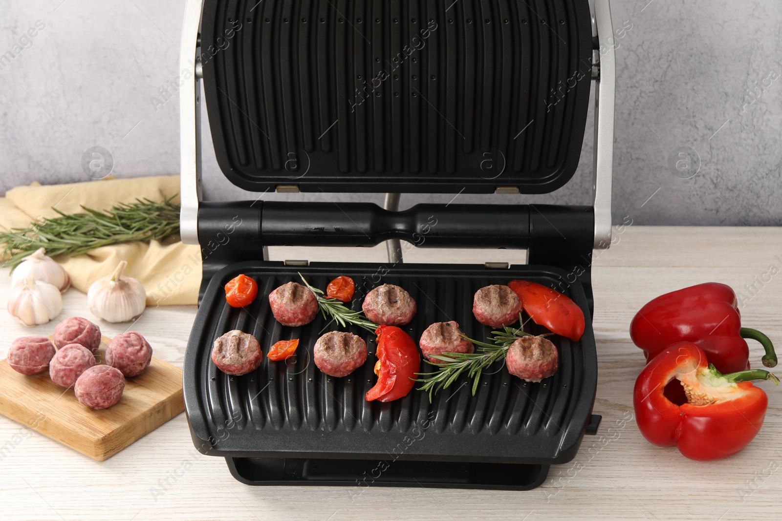 Photo of Electric grill with vegetables, meat balls and rosemary on wooden table