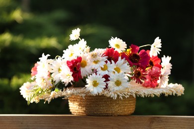 Photo of Beautiful wild flowers in wicker basket on wooden table against blurred background