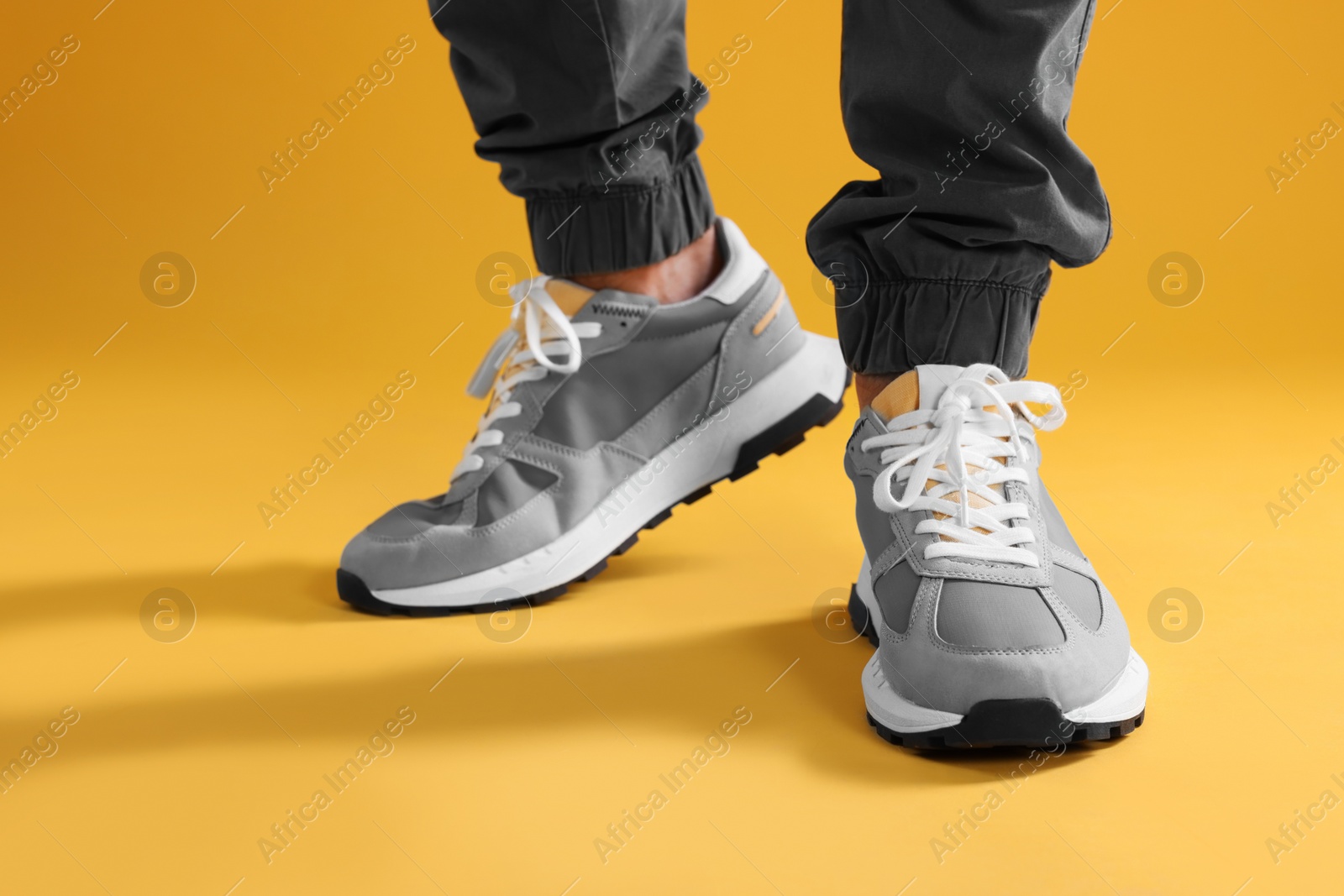 Photo of Man wearing stylish sneakers on yellow background, closeup