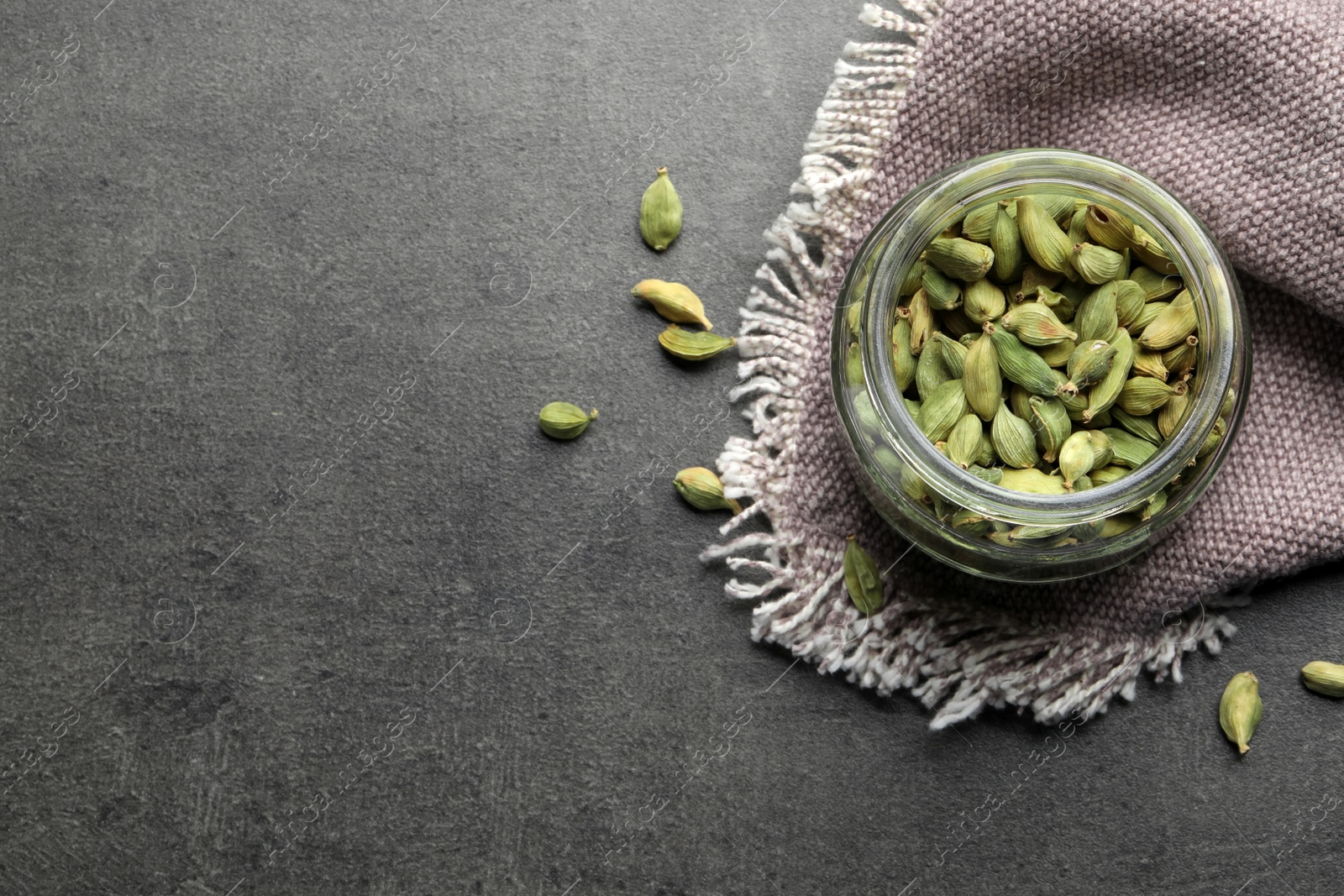 Photo of Jar with dry cardamom pods on dark grey table, flat lay. Space for text