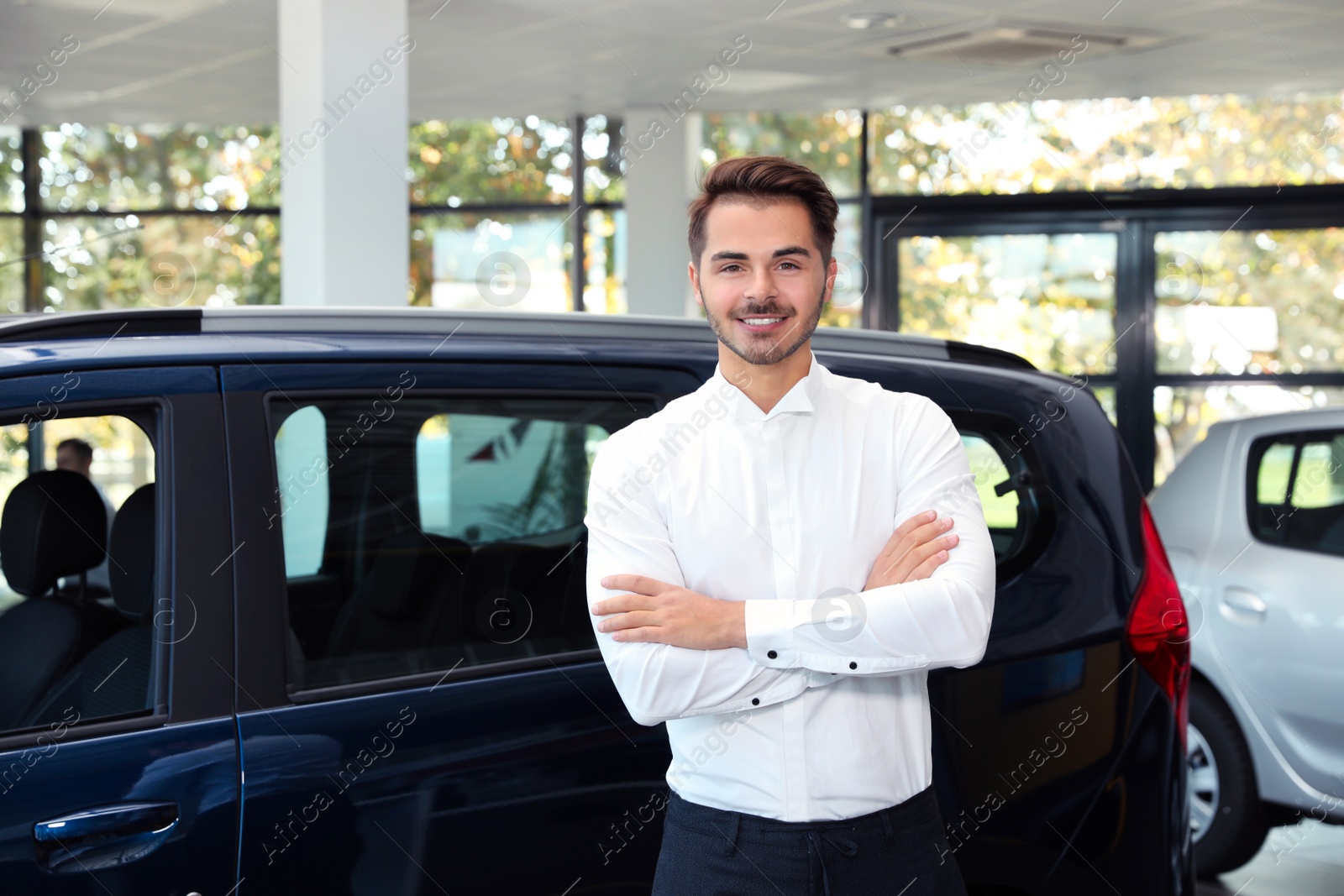 Photo of Young man near new car in dealership