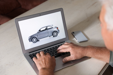 Photo of Man using laptop to buy car at wooden table indoors, closeup