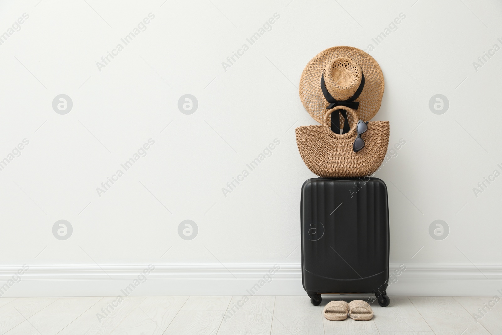 Photo of Packed suitcase, shoes and summer accessories near white wall indoors. Space for text