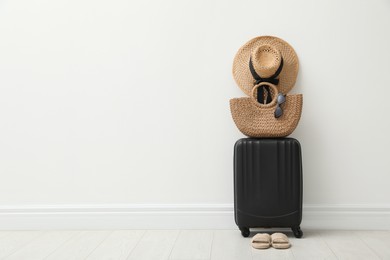 Photo of Packed suitcase, shoes and summer accessories near white wall indoors. Space for text