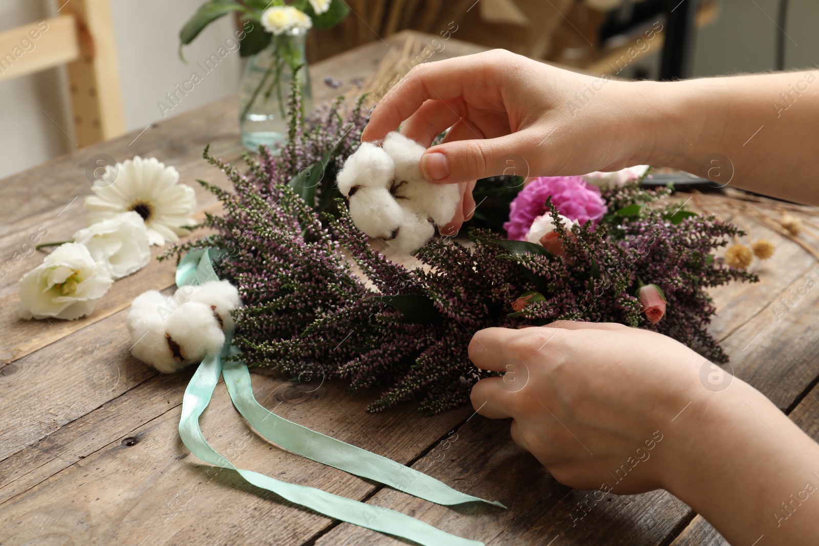 Photo of Florist making beautiful autumnal wreath with heather flowers at wooden table, closeup