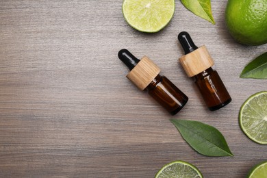 Bottles of essential oil with lime slices and leaves on wooden table, flat lay. Space for text
