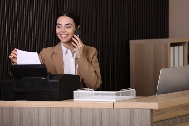 Photo of Receptionist talking on smartphone at countertop in office