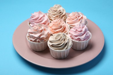 Photo of Plate with tasty cupcakes on light blue background, closeup