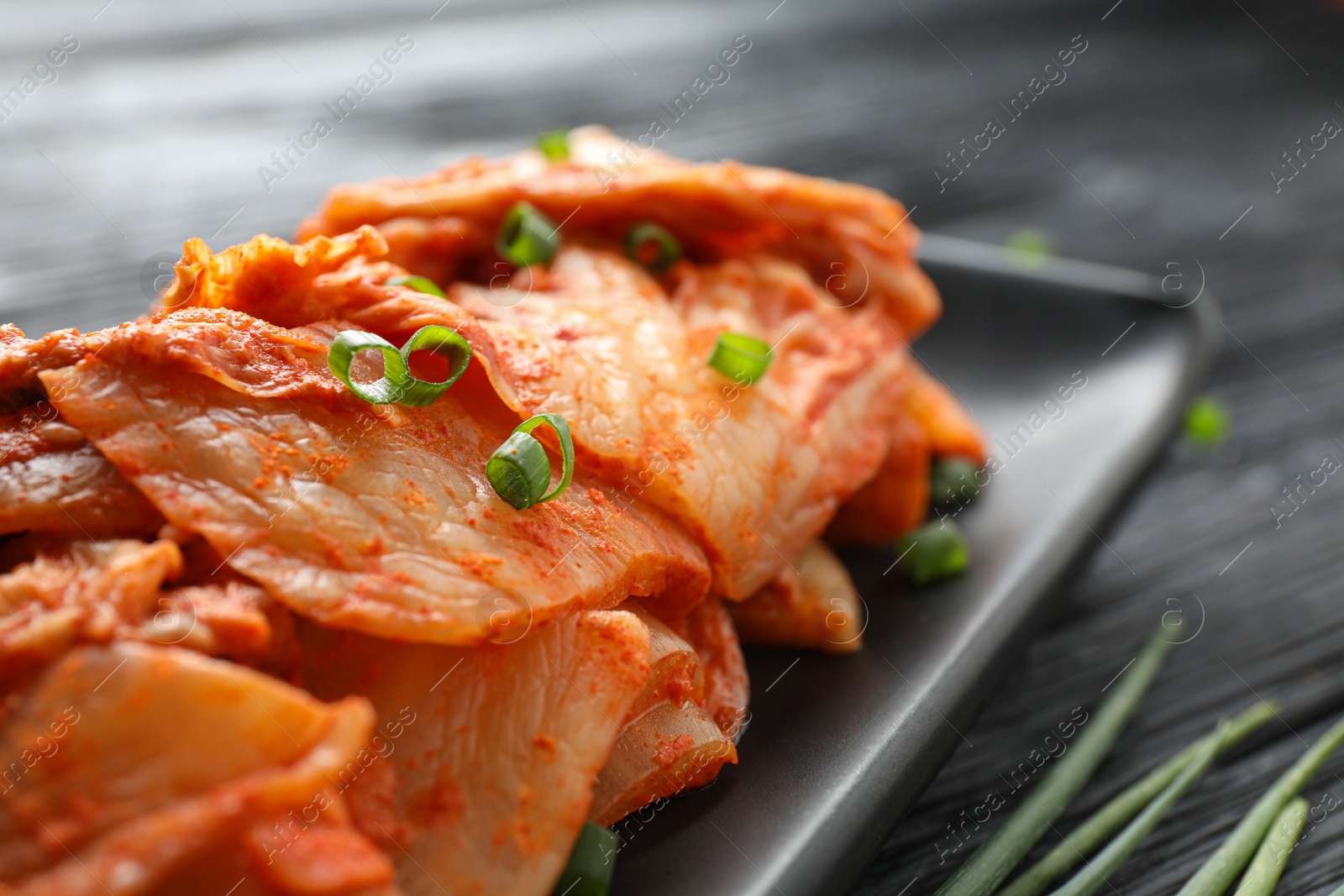 Photo of Delicious kimchi with Chinese cabbage and green onion on black wooden table, closeup