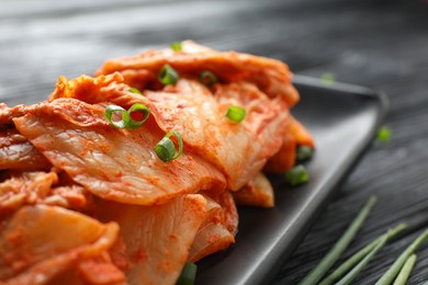 Delicious kimchi with Chinese cabbage and green onion on black wooden table, closeup