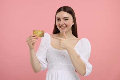 Happy woman pointing at credit card on pink background