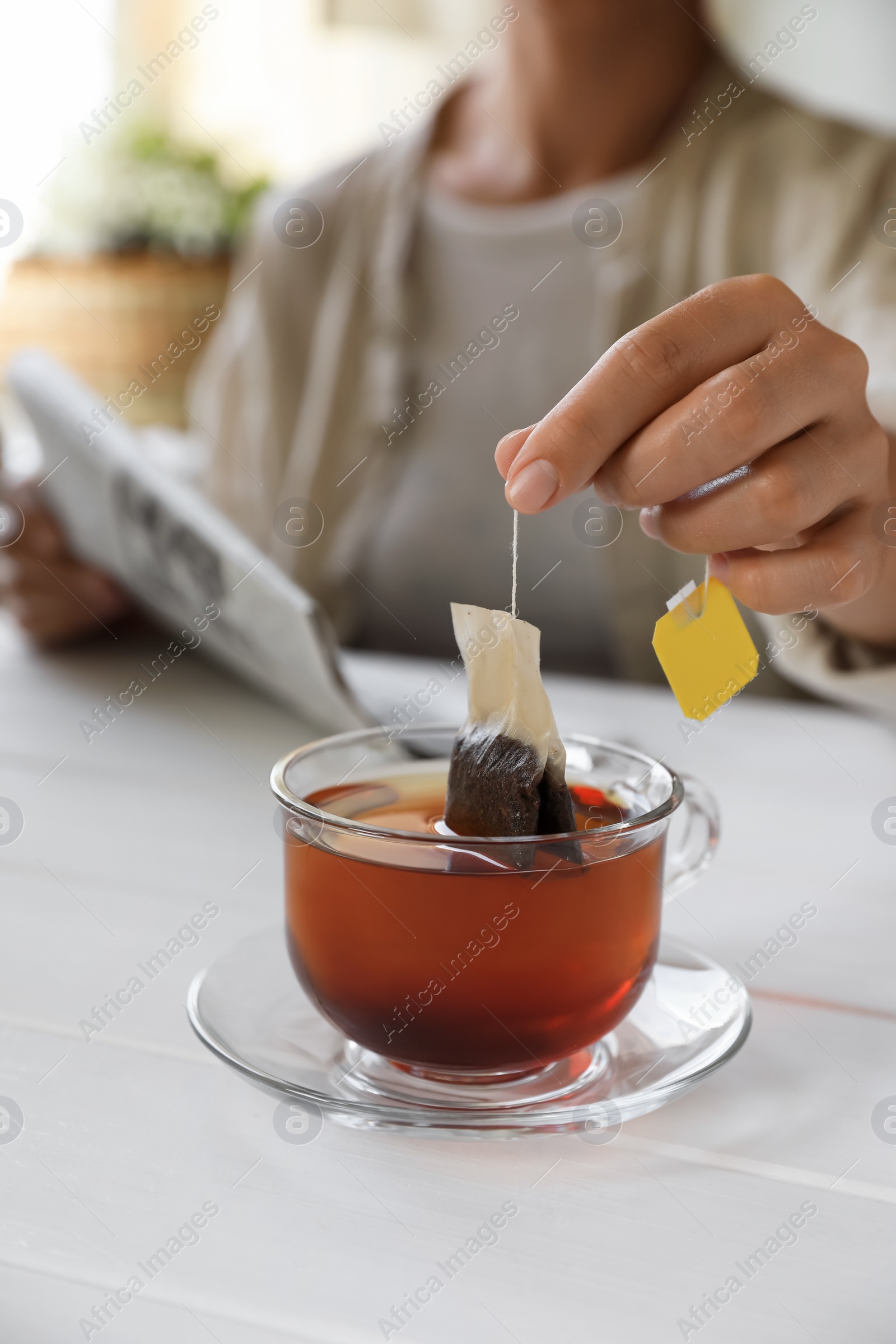 Photo of Woman taking tea bag out of cup at white wooden table indoors, closeup