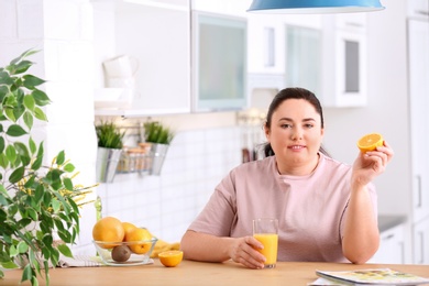 Photo of Overweight woman with glass of fresh juice and orange in kitchen. Healthy diet