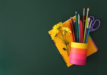 Photo of Different school stationery and beautiful yellow flowers on green chalkboard, flat lay with space for text. Happy Teacher's Day