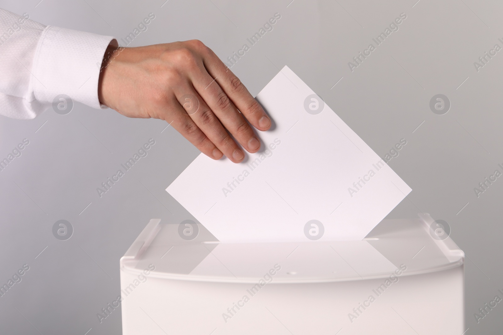 Photo of Man putting his vote into ballot box on light grey background, closeup