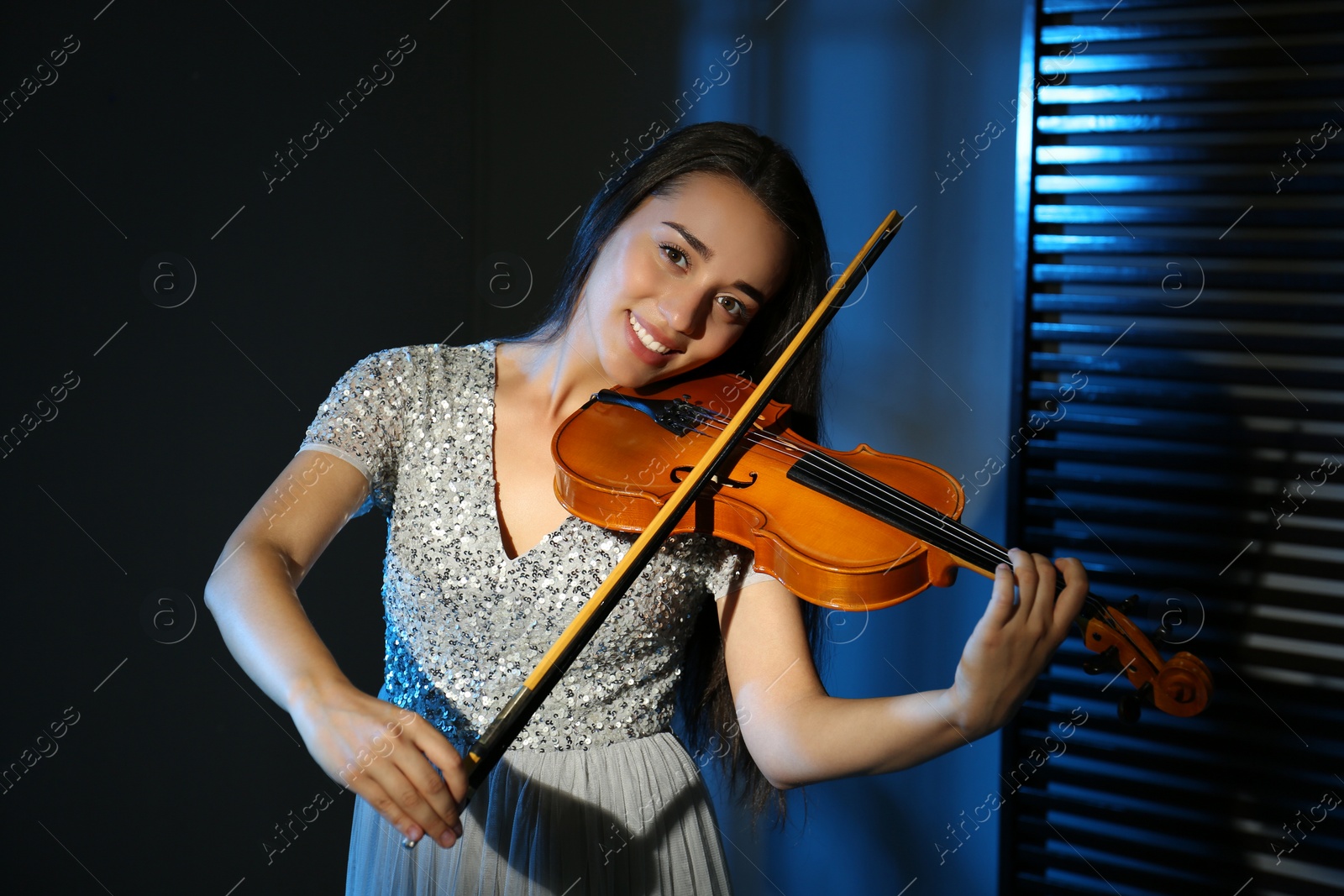 Photo of Beautiful young woman playing violin in dark room
