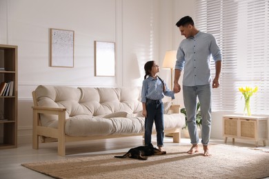 Photo of Father and daughter with puppy near sofa in living room