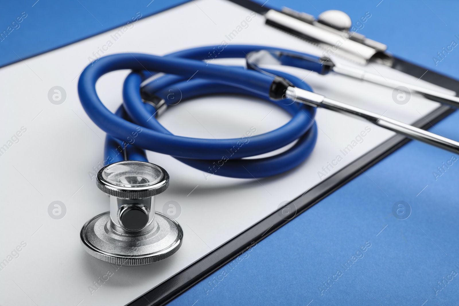 Photo of Clipboard with stethoscope on blue background, closeup