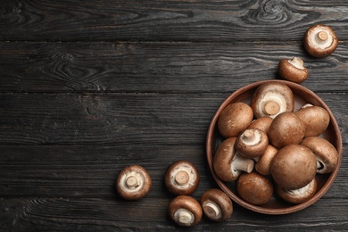 Photo of Bowl with fresh champignon mushrooms on wooden table, top view. Space for text